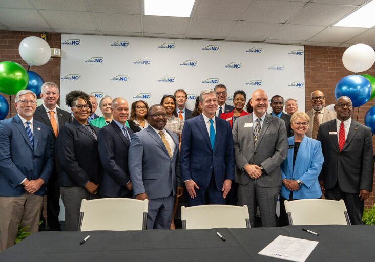 Gov. Roy Cooper (center, front row) and North Carolina Community College System President Dr. Jeff Cox (third from right, front row) stand with the presidents of 10 North Carolina community colleges, including Randolph Community College President Dr. Shah Ardalan (back row, center), presidents of N.C. A&T State University and N.C. State University, and six workforce development board representatives Thursday, Sept. 21, at Central Carolina Community College’s Eugene Moore Manufacturing and Biotech Solutions Center at a signing event for the AdvanceNC charter.
